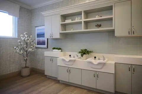 Room with two hair-washing basins, white cupboards and a framed landscape picture
