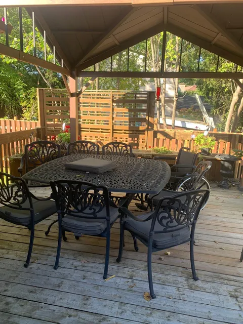 Covered wooden deck with a metal dining table, chairs and garden beyond