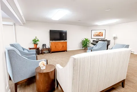 Armchairs and a sofa facing a blank television beside a piano