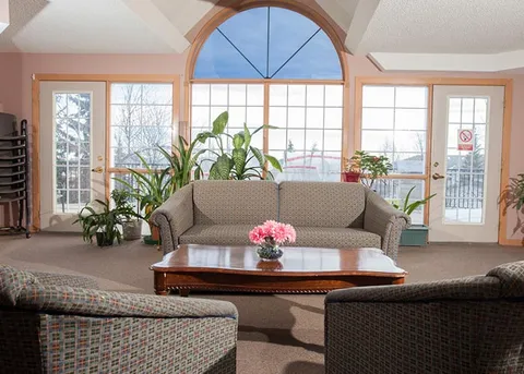 Lounge with a sofa, armchairs and plants beside a tall arched window.