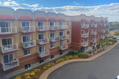Apartment building with balconies, flower beds and a curved driveway.