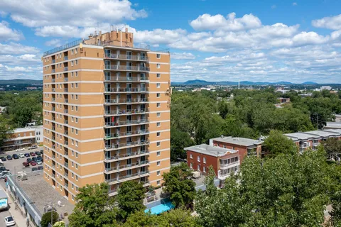 Aerial view of a tall brick building with balconies and surrounding trees