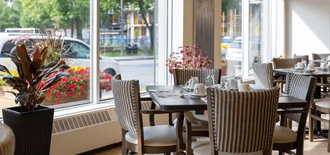 Dining tables and upholstered chairs beside tall windows