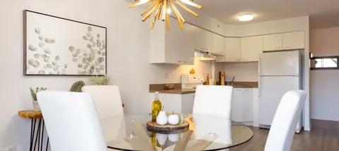 Dining table with white chairs beside a compact white kitchen