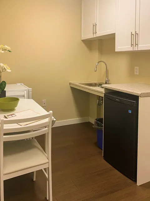 Kitchenette with a sink, white cabinets, small refrigerator and white dining table
