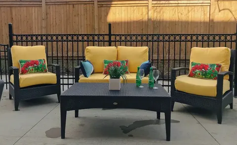 Patio seating with yellow cushions beside a black railing and wooden fence