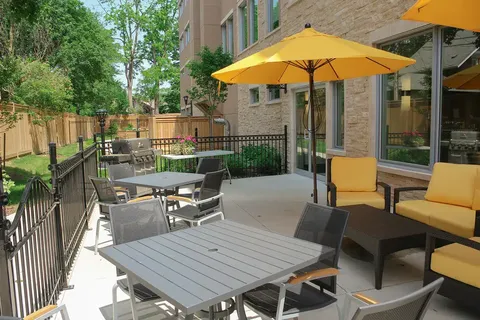 Patio with tables, metal chairs, yellow umbrellas and a barbecue beside the building