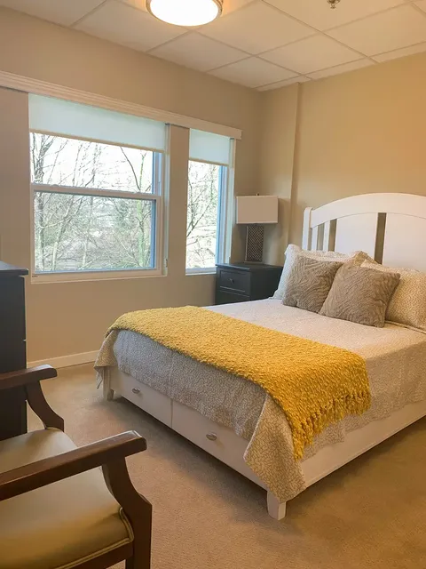 Bedroom with a white bed, yellow blanket, bedside lamp and two windows