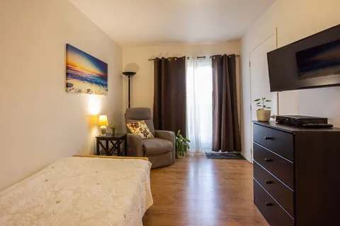 Bedroom with an armchair, dresser, television and a beach painting