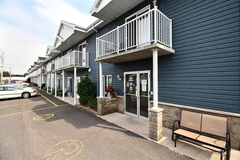 Blue building with white balconies, parked cars and a bench beside the entrance