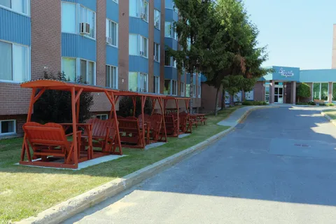 Residence exterior beside a driveway and a row of covered wooden swings