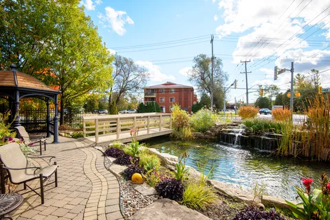 Garden pond with a small waterfall, a bridge, patio chairs and flower beds