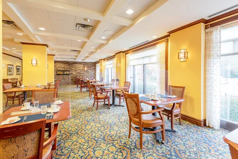 Dining tables and chairs beside large windows, yellow walls and patterned carpet