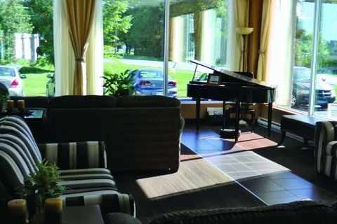 Window-side sitting room with a piano and striped chairs.