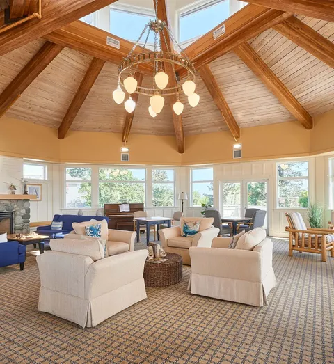 Lounge with white upholstered chairs, a wood ceiling, chandelier and large windows.