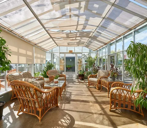 Sunroom with wicker chairs and tables, potted plants and a glass roof.
