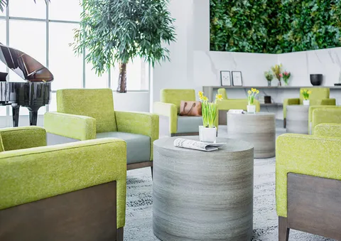 Green armchairs and round side tables beside a grand piano and a plant wall