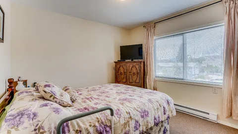 Suite bedroom with a bed, dresser and large window.
