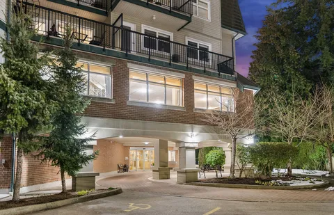 Illuminated residence entrance and landscaped front drive at dusk