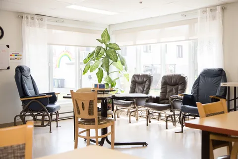 Sitting area with padded armchairs, tables, large windows and plants