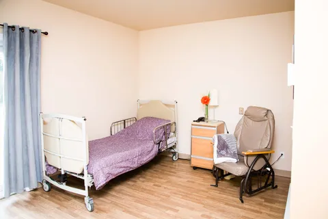 Bedroom with an adjustable bed, purple bedding, an armchair and bedside cabinet