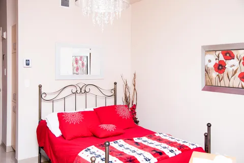 Bed with red pillows beneath a mirror and floral wall pictures