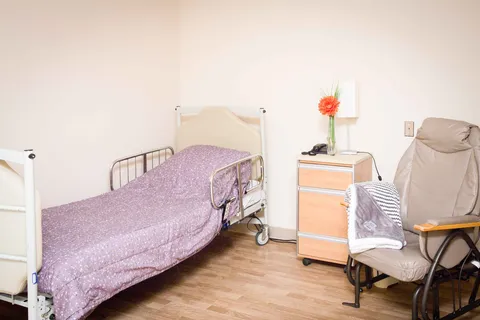 Adjustable bed with purple bedding beside a cushioned armchair and bedside cabinet