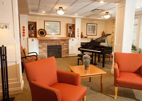 Lounge with a grand piano, fireplace and orange armchairs.