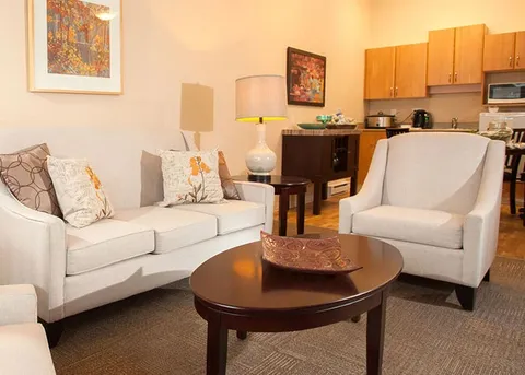 Suite living area with a kitchenette and white seating.
