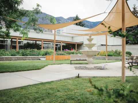 Courtyard with shade sails, a tiered fountain, benches, lawn and planted beds.