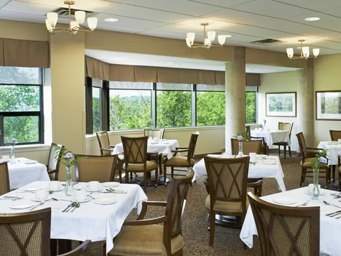 Dining room with white tablecloths and windows overlooking trees