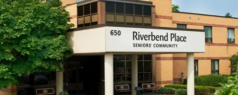 Brick building with a covered entrance, benches and a Riverbend Place sign