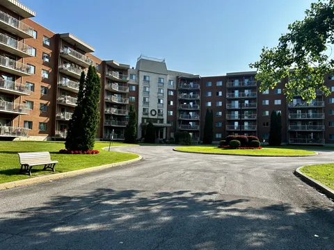 Brick residence with balconies, a circular drive, lawns and a bench