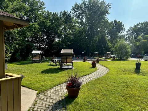 Garden with a curved paved path, covered swings, flower pots and picnic tables