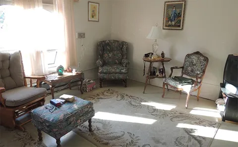 Sunlit room with armchairs, side tables and a rug.