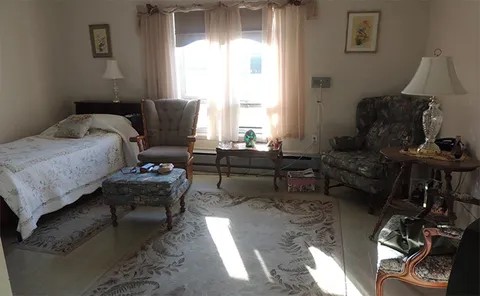 Furnished bedroom with a bed, armchairs and a curtained window.