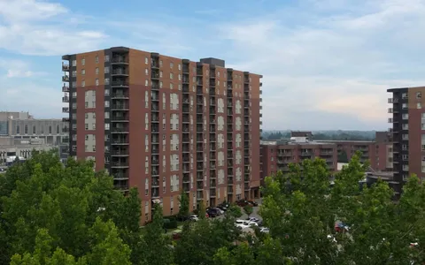 Brick residence tower with balconies and trees below.