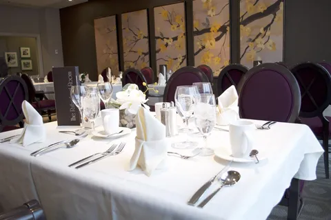 Dining room table set with glasses, plates and folded napkins beside purple chairs.