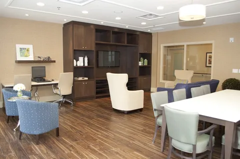 Common lounge with armchairs, tables, a television and built-in cabinets.