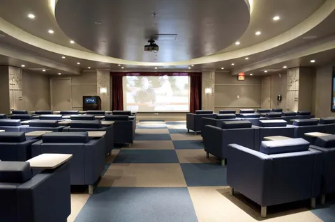 Theatre room with rows of armchairs, side tables and a projection screen.