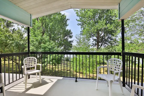 Covered balcony with white chairs, black railings and a view of trees