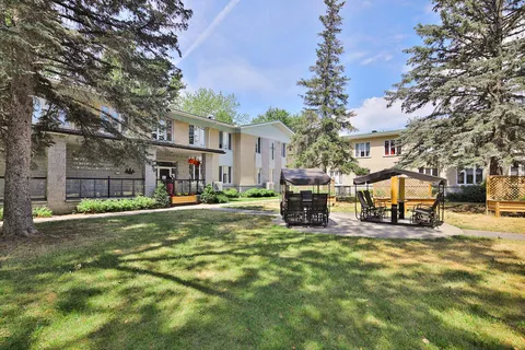 Building behind a lawn, trees and two covered seating areas