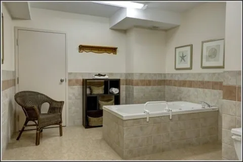 Bathing room with a tub, vanity, grab bar and chair.