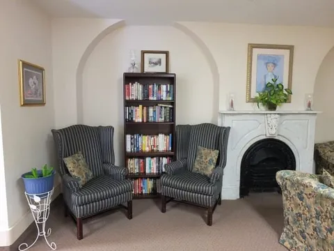 Library sitting area with bookshelves, armchairs and a fireplace.