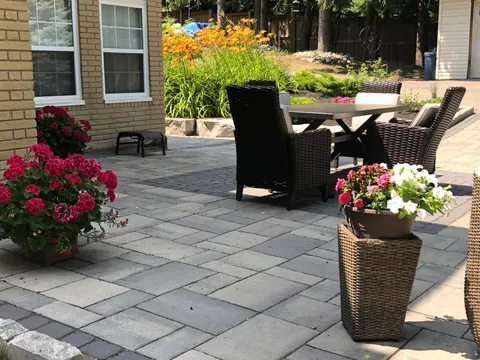 Paved patio with wicker chairs, a dining table and flower planters
