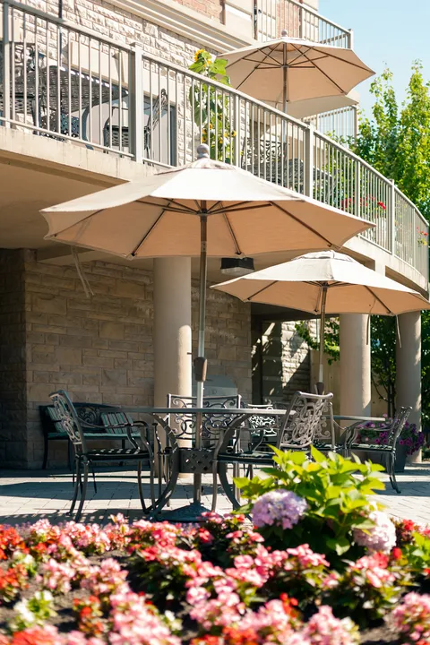 Patio seating and umbrellas beside flowering beds.