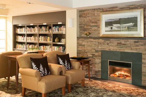 Library seating beside a stone fireplace and bookshelves.
