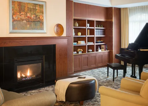 Fireside lounge with a piano, shelving and upholstered seating.