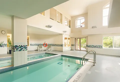 Indoor swimming pool with tall windows and metal entry rails.