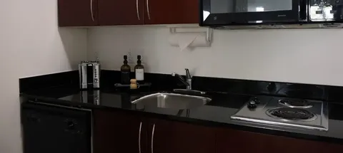 Kitchenette with dark cabinets, sink, microwave and stovetop.